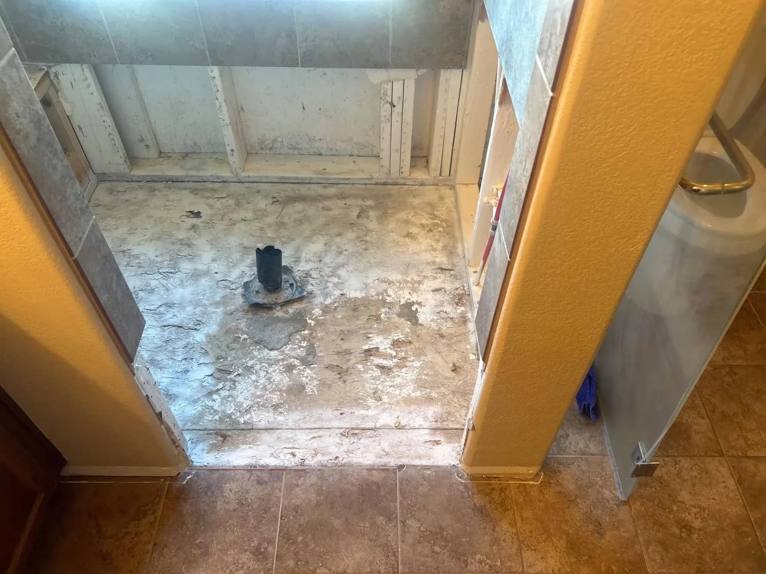 An Aurora shower floor before repair shows a damaged surface and an exposed drain.