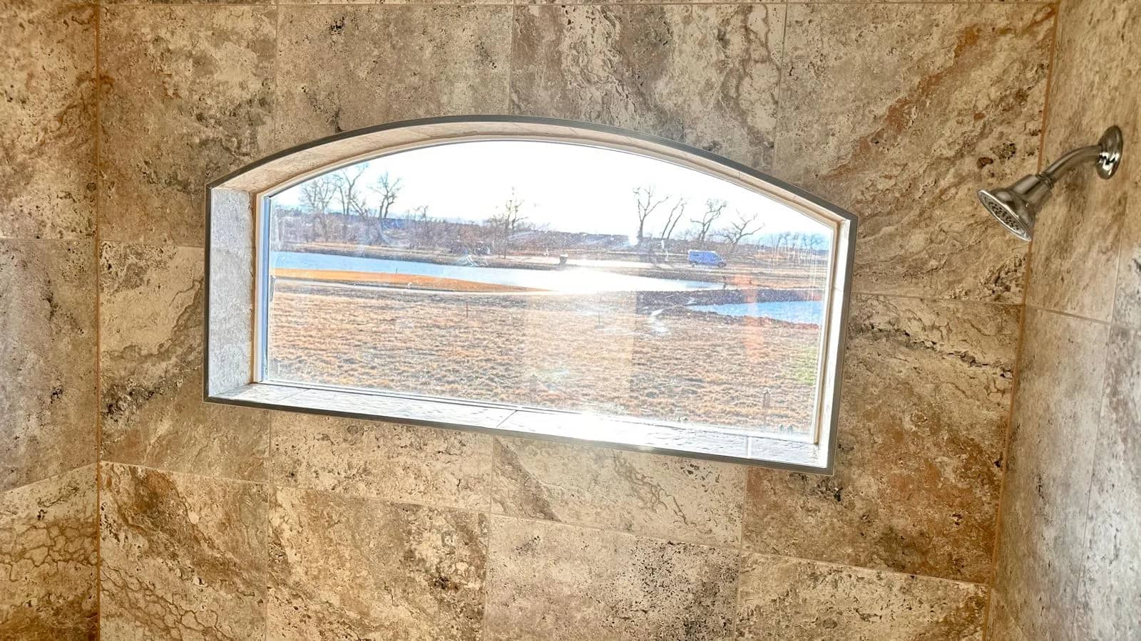 Tan wall tile surrounds an arched window in an Aurora shower.