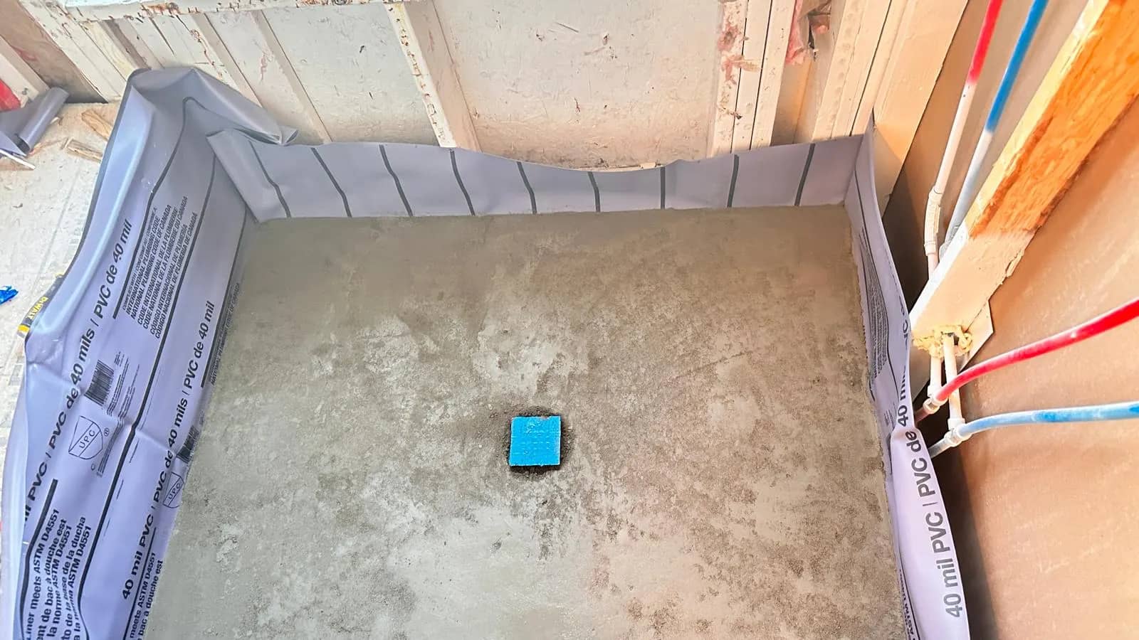 A gray shower base in Aurora is surrounded by a purple liner turned up at the walls during installation.