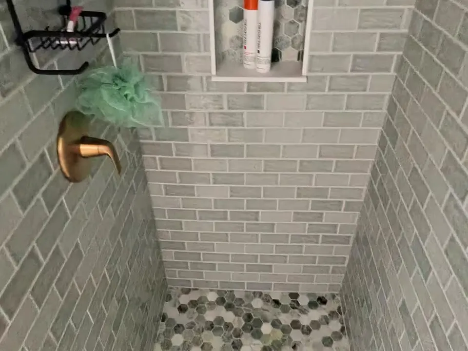 A Denver shower has gray rectangular wall tile, a hexagon-tile floor, and a recessed niche with toiletries.