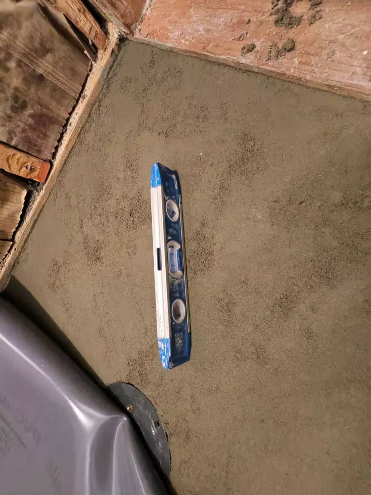 A level rests on a fresh gray mortar shower bed in Denver beside a gray liner.