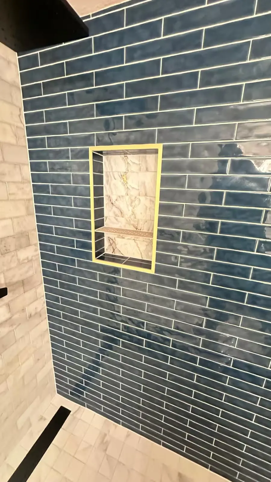 Blue rectangular wall tile surrounds a small marble-look recessed niche in an Aurora basement shower.