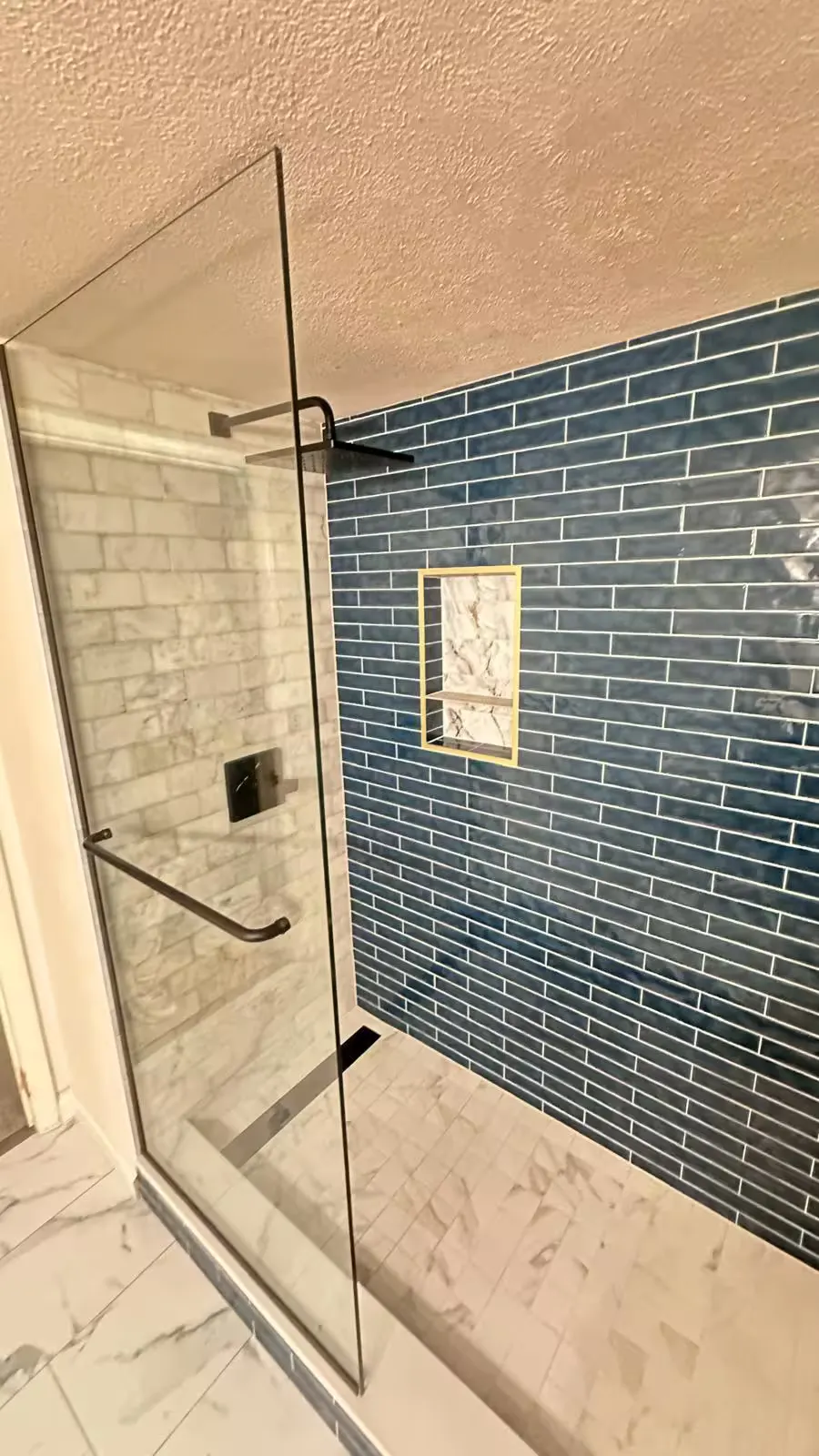 A glass shower door with dark hardware opens toward blue rectangular tile in an Aurora basement bathroom.