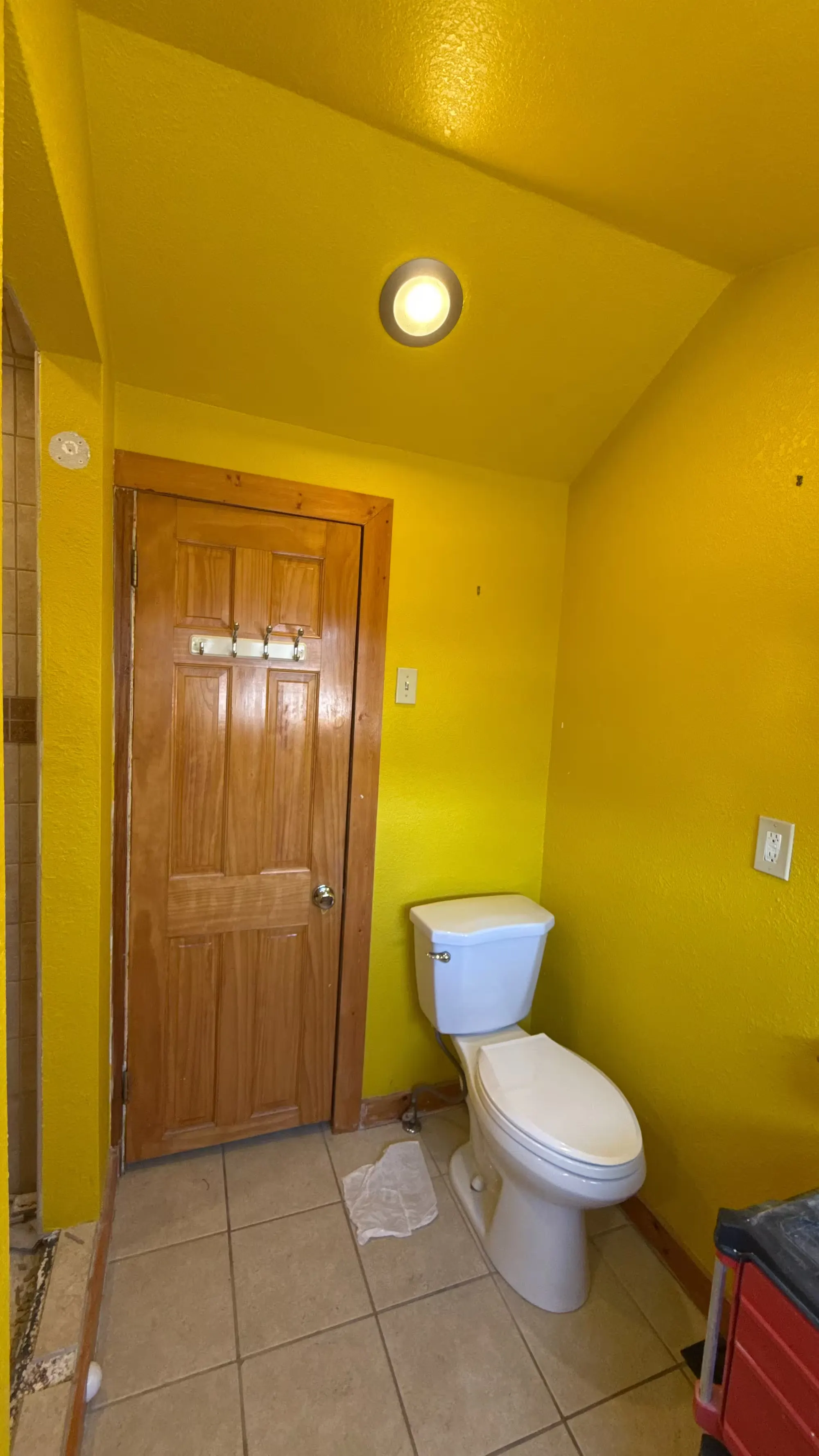 A yellow Denver bathroom before remodeling has a wood door, a toilet, and beige floor tile.
