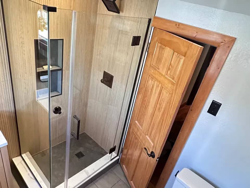 A Denver bathroom after a shower remodel shows beige vertically ridged wall tile, a glass enclosure, and black fixtures.