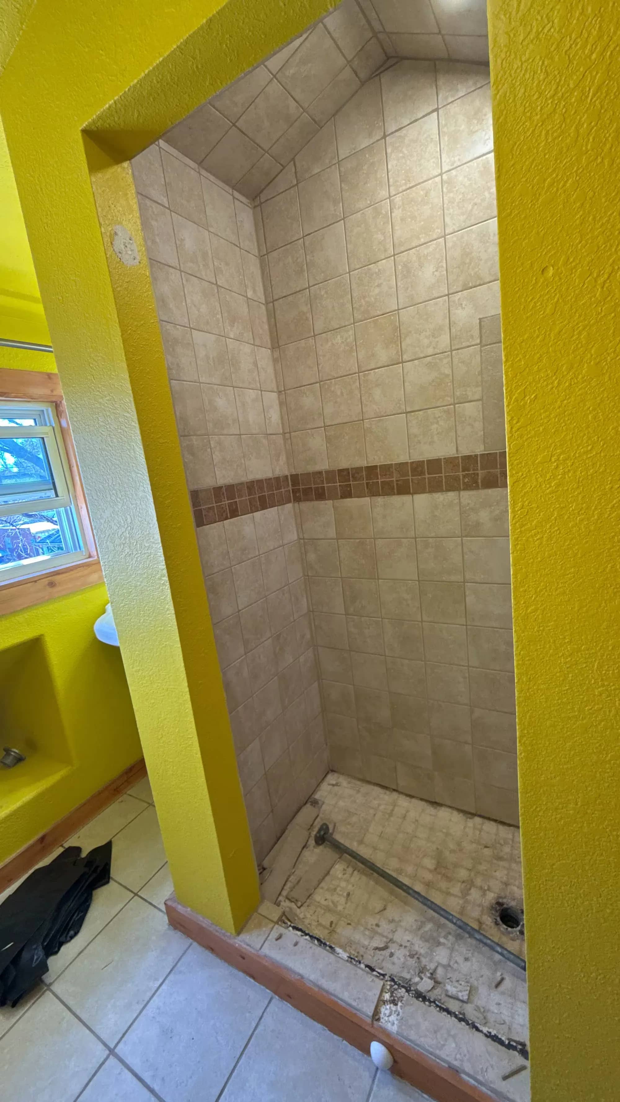 A Denver shower during wall rebuilding has a window, plain upper walls, and a horizontal band of beige tile.