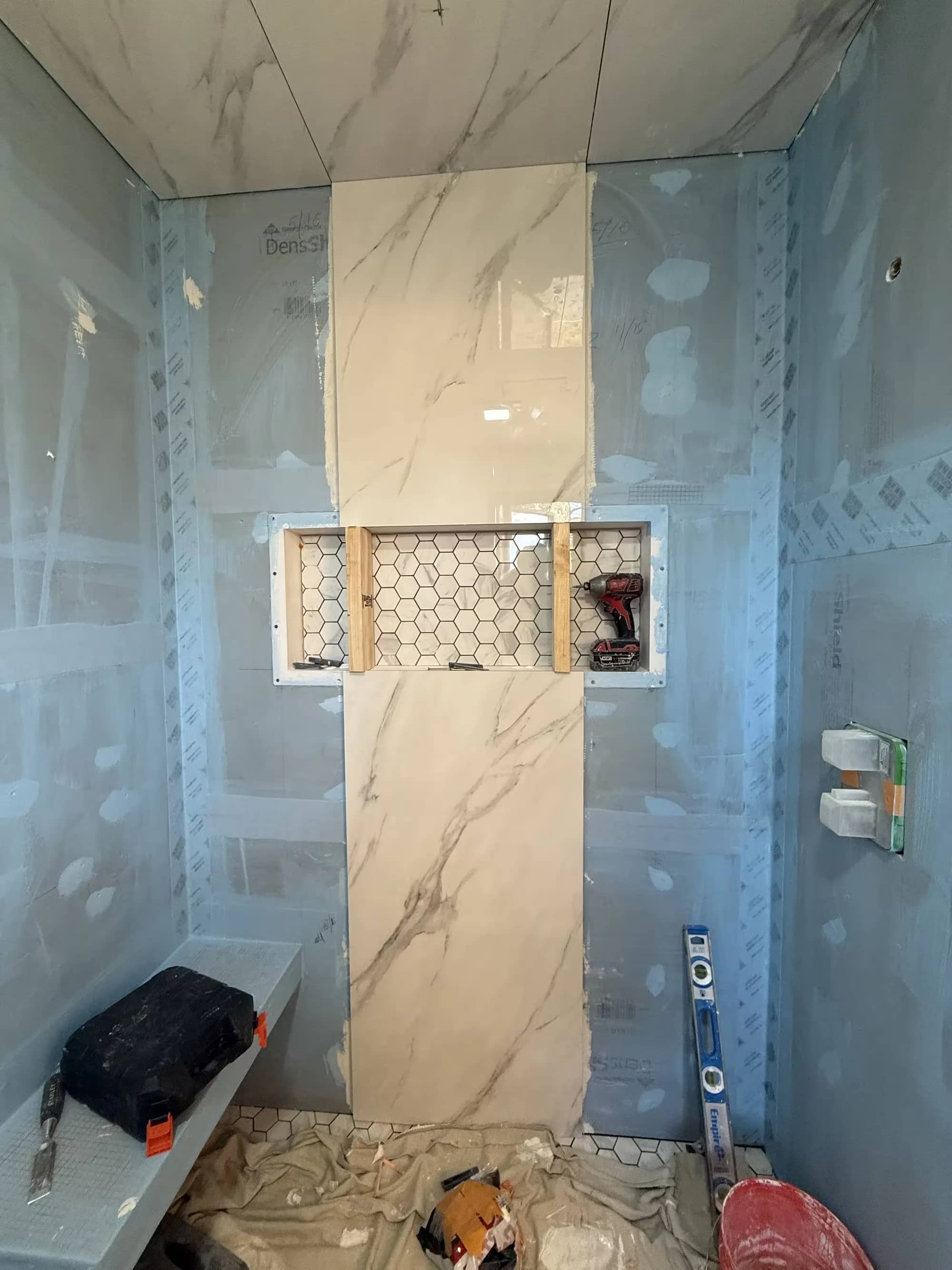 A Littleton shower during preparation has blue wall boards, a partially tiled wall, and a recessed niche.