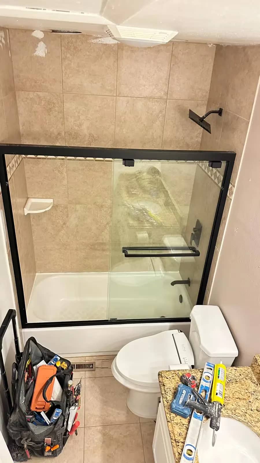 An Aurora bathroom before remodeling has a beige-tile tub and shower enclosure beside a toilet.
