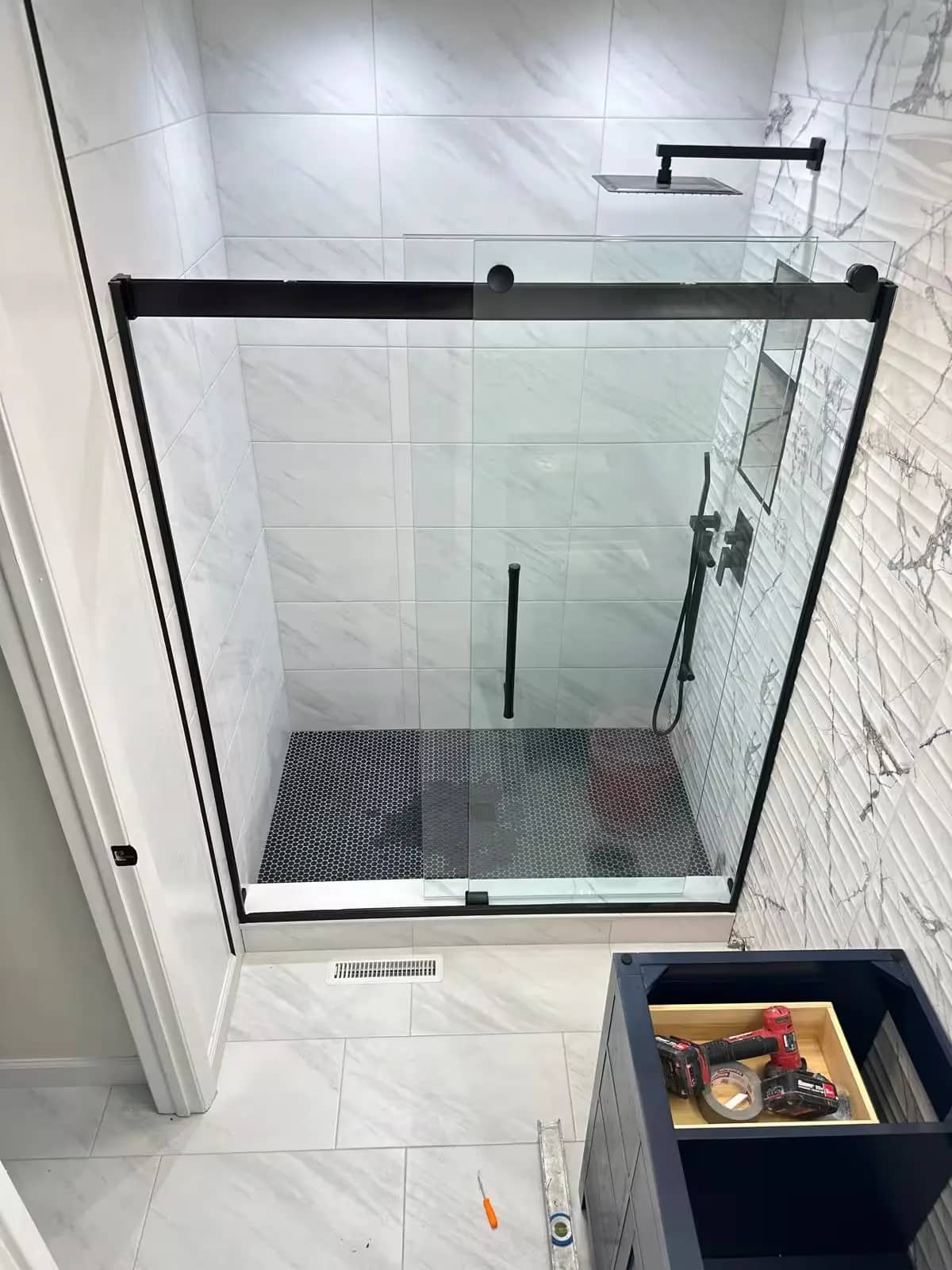 A black-framed glass shower front encloses light marble-look wall tile and a dark floor in an Aurora bathroom.