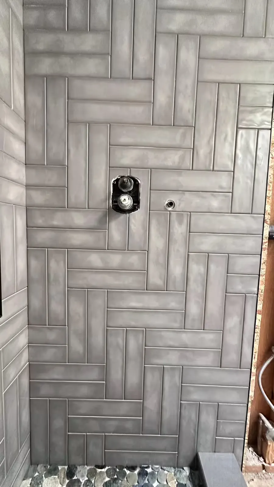 A close-up shows gray herringbone shower wall tile around fixture openings during an Arvada remodel.