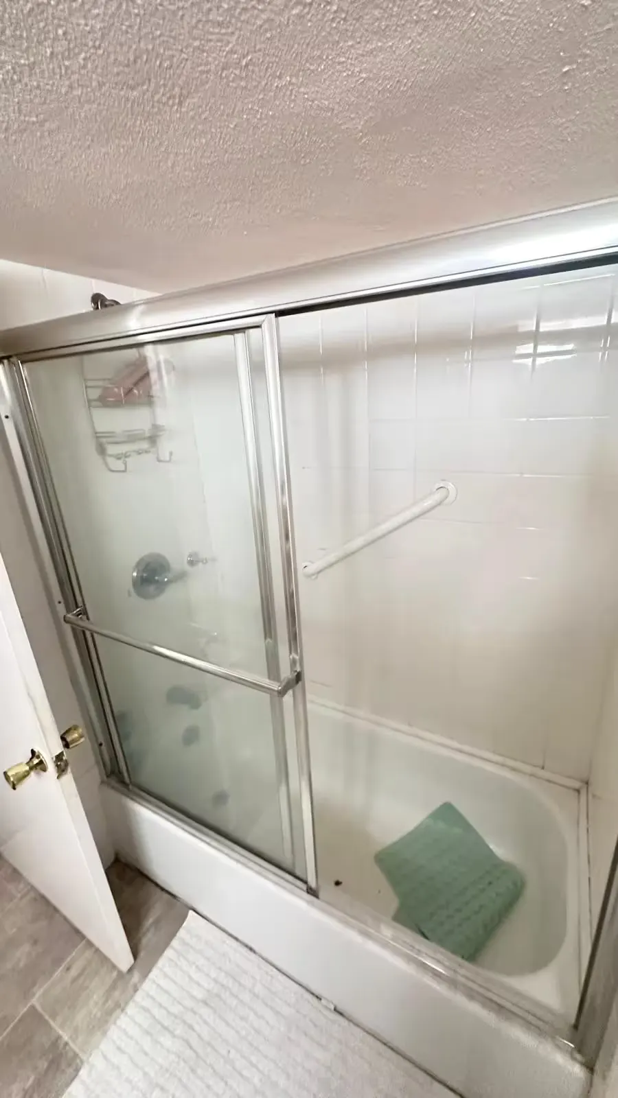 An Aurora basement bathtub with a sliding glass enclosure sits beneath a showerhead before conversion.