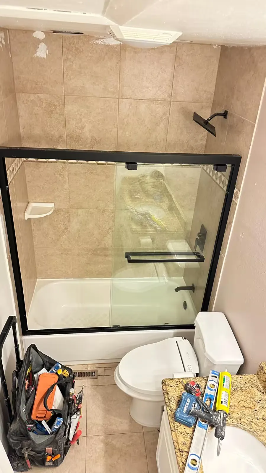 An Aurora bathroom before remodeling has a beige-tile tub and shower enclosure beside a toilet.