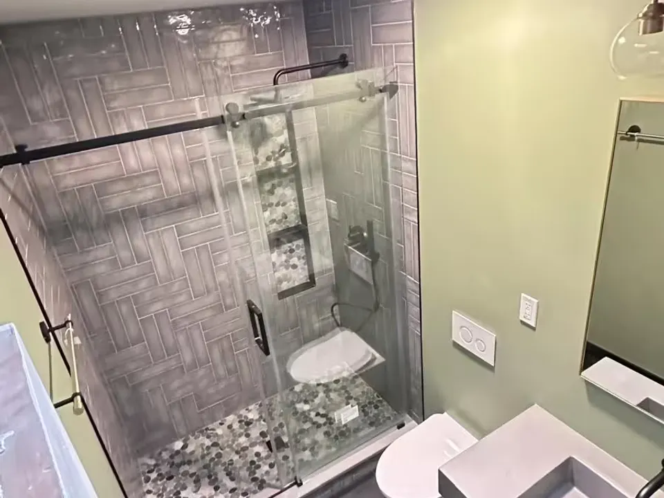 A remodeled Arvada bathroom has a glass-enclosed walk-in shower beside a wall-hung toilet and a custom concrete sink.