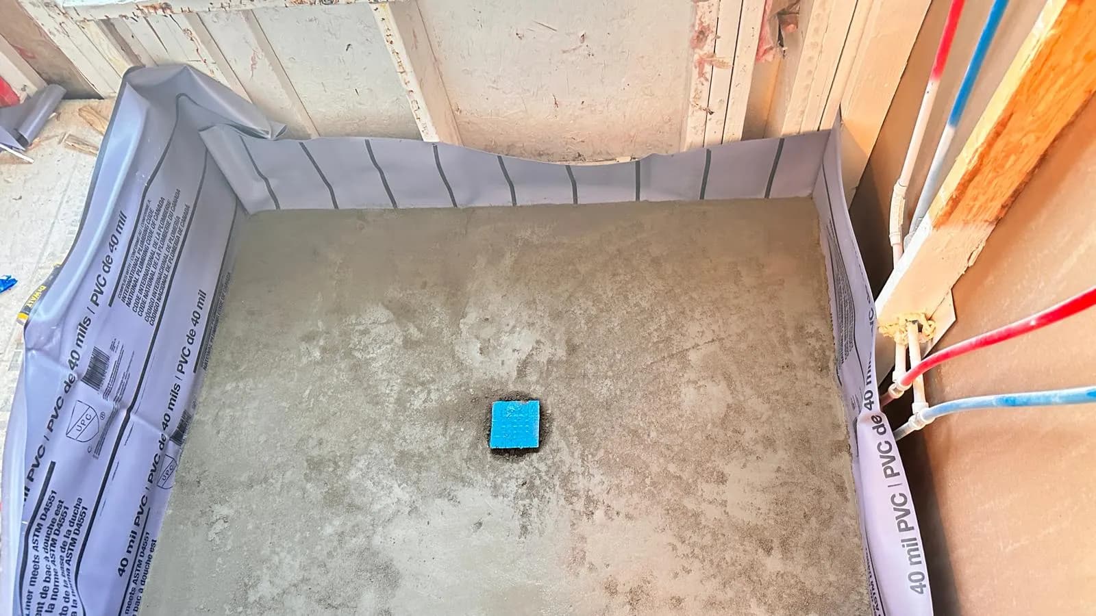 A gray shower base in Aurora is surrounded by a purple liner turned up at the walls during installation.