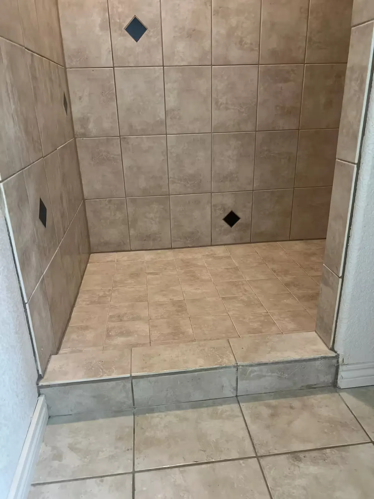 The entrance to an Elizabeth shower before repair has beige floor tile and a tiled threshold.