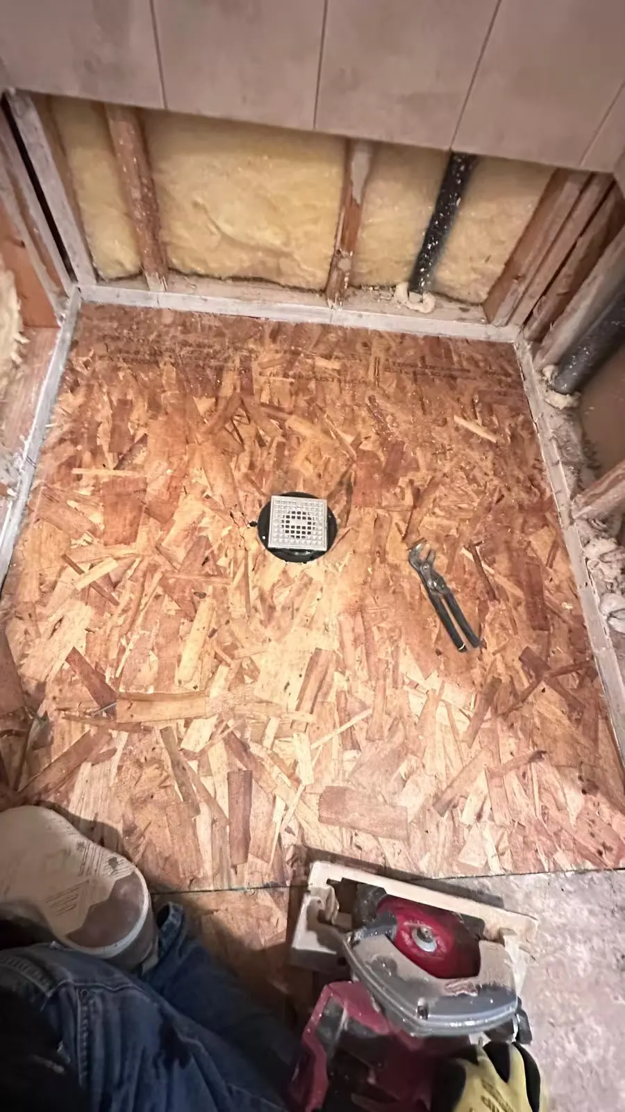 Exposed OSB subfloor panels surround a central drain in an Elizabeth shower during reconstruction.