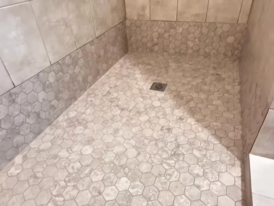 An Elizabeth shower after renovation has beige wall tile and a hexagon-tile floor.
