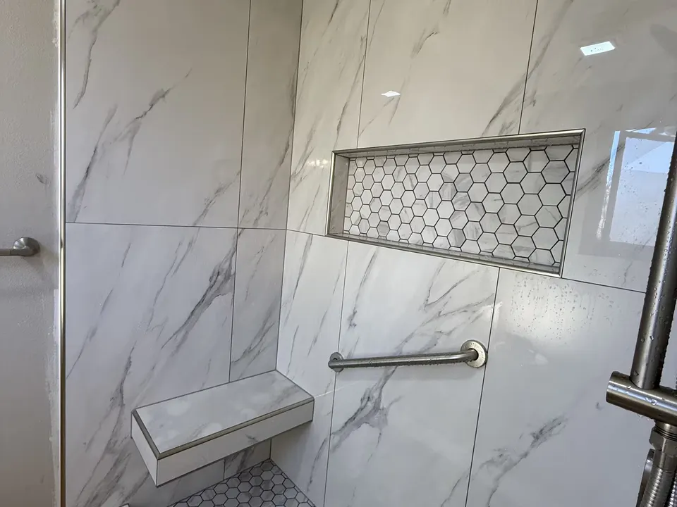 A Littleton shower has marble-look wall tile, a floating bench, a hexagon-tile floor, and a recessed niche.