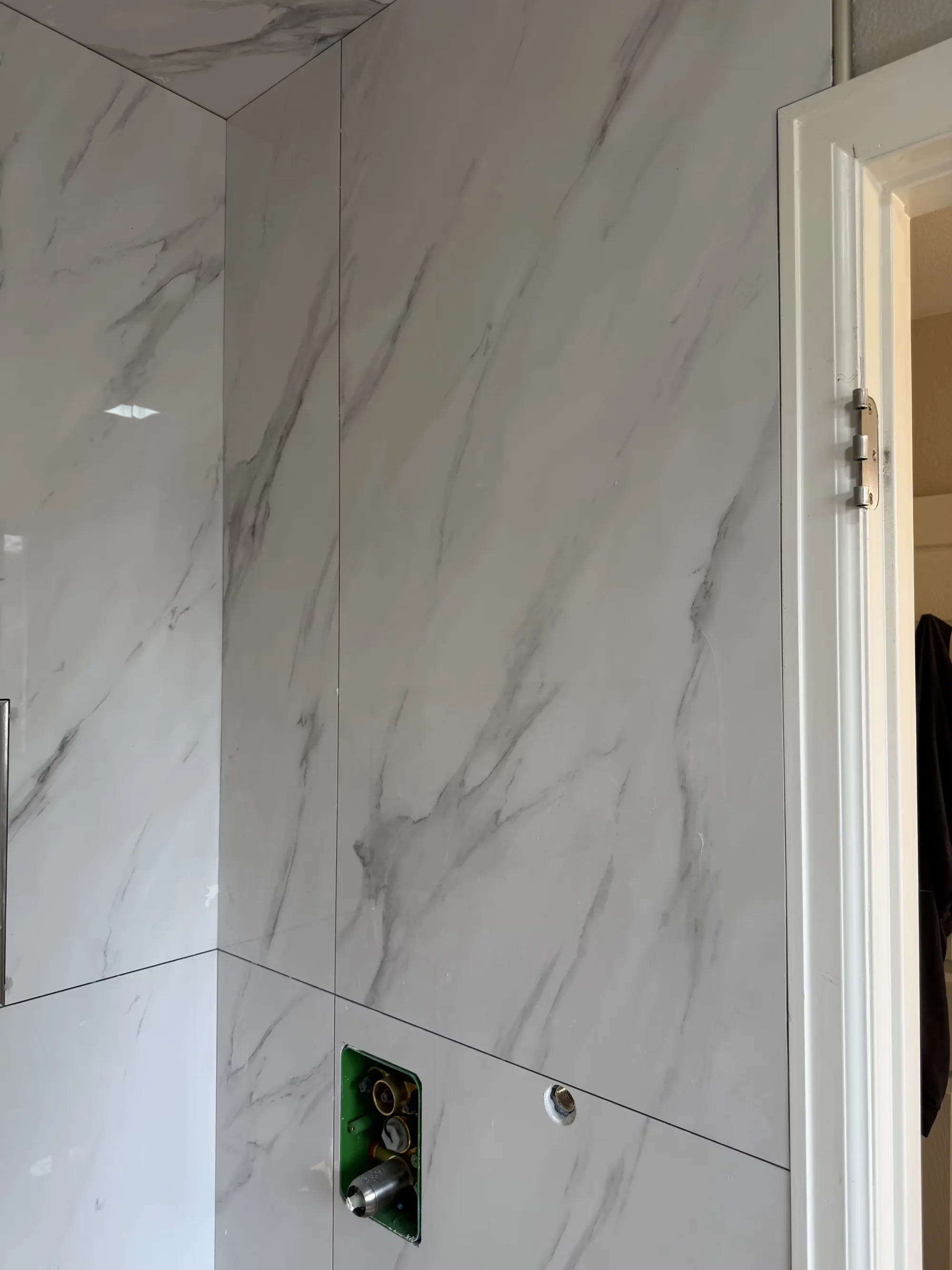 Large marble-look wall tiles meet a vertical edge beside a fixture opening in a Littleton shower.